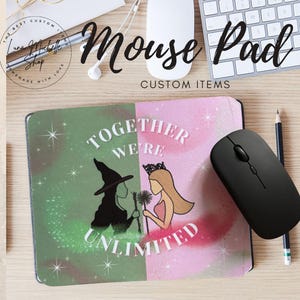 May include: A green and pink mouse pad with a design of two women, one with a witch's hat and the other with a crown. The text "Together We're Unlimited" is printed on the mouse pad.