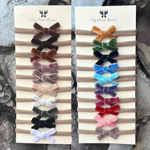 May include: Two cards with a variety of velvet bows on nude nylon headbands. The cards are labeled "Tiny Miracles Boutique".