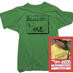 Puede incluir: Camiseta verde con una ilustraci&oacute;n en blanco y negro de una portada de libro que dice "Fear and Loathing". La camiseta tiene una peque&ntilde;a etiqueta con el texto "Fear and Loathing" y la fecha "1985". La etiqueta tambi&eacute;n dice "Hunter S. Thompson" y "Colorado".
