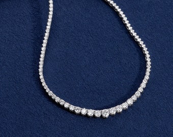 May include: A delicate diamond tennis necklace with a silver chain. The necklace is laid out on a pink and blue fabric background.