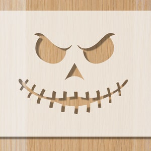 Könnte beinhalten: Eine hellfarbene Holzschablone mit einem geschnitzten Halloween-Gesicht. Das Design umfasst angewinkelte Augen, eine dreieckige Nase und einen Mund mit Steppstich. Die Schablone wird wahrscheinlich zum Basteln oder Dekorieren verwendet.