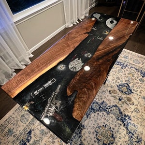 May include: A dark wood table with a black epoxy resin top featuring a galaxy design with stars, planets, and spaceships. The table is approximately 1.8 metres long and 0.9 metres wide.
