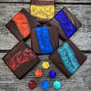 May include: A set of six square coasters made of dark wood with colourful resin inserts. The coasters feature a variety of colours, including red, orange, yellow, blue, green, and turquoise. The coasters are arranged in a diamond shape on a wooden surface. There are six small hexagonal resin pieces in various colours below the coasters.