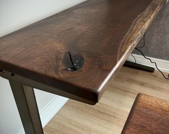 May include: A dark brown wooden desk with a live edge top and a black metal adjustable frame. The desk is sitting on a light brown wood floor.