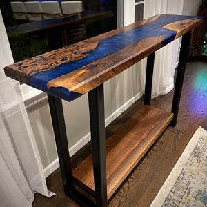 May include: A walnut wood console table with a blue epoxy river design and a lower shelf. The table has a black metal frame.