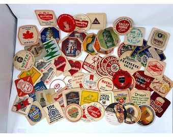 May include: A large collection of assorted cardboard beer coasters in various shapes, sizes, and colors. The coasters feature diverse graphic designs, brand logos, and text including Yuengling, Molson, Guinness, Beck's, and Tecate, scattered across a surface.