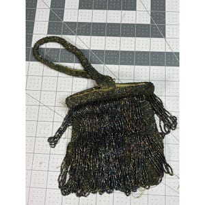 May include: A vintage beaded handbag with a looped handle and long fringe. The bag is primarily black with iridescent green and gold beads. The handle and top of the bag are also beaded.