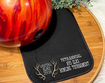 May include: A black bowling ball mat with white embroidery. The text reads "75th Annual NYS Elks Bowling Tournament" and "Vestal Elks 2508".