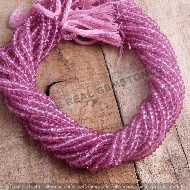 May include: A strand of pink faceted gemstone beads. The beads are small and round, and they are strung on a thin wire. The beads are arranged in a circle, and they are all the same size and shape.