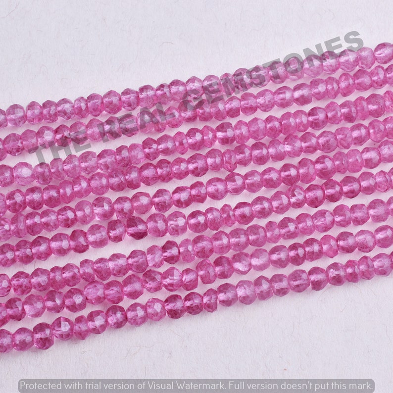 May include: A strand of pink faceted gemstone beads. The beads are small and round, and they have a translucent appearance.