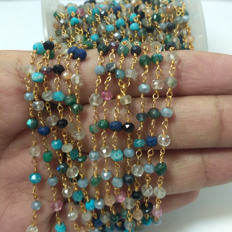 Op de afbeelding: Een veelkleurige edelsteenketting met goudkleurige metalen schakels. De ketting is gemaakt van verschillende edelstenen, waaronder turquoise, lapis lazuli en smaragd.