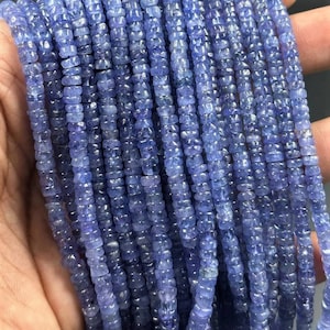 May include: A strand of blue gemstone beads, each bead is faceted and has a square shape. The beads are strung together on a clear thread.