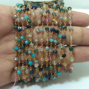 Op de afbeelding: Een meerstrengs ketting met kleine, kleurrijke edelsteen kralen en gouden kettingschakels. De kralen zijn in verschillende tinten blauw, groen, roze en wit.