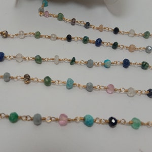 Op de afbeelding: Een gouden ketting met verschillende gekleurde edelsteen kralen, waaronder turquoise, groen, roze en blauw.