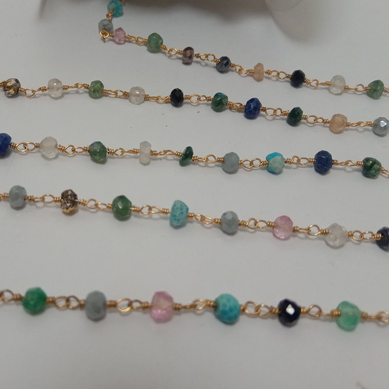 Op de afbeelding: Een gouden ketting met verschillende gekleurde edelsteen kralen, waaronder turquoise, groen, roze en blauw.