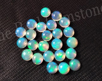 May include: A selection of round opals with an iridescent sheen. The opals exhibit a spectrum of colours, including blue, green, and yellow, set against a milky white backdrop. The gemstones are arranged on a dark, textured surface.
