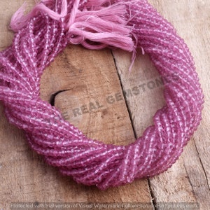 May include: A strand of pink faceted gemstone beads. The beads are small and round, and they are strung on a thin wire. The beads are arranged in a circle, and they are all the same size and shape.