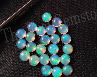 May include: A collection of 25 round, iridescent opal cabochons. The opals are a light blue-green color with flashes of rainbow.
