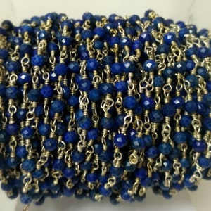 May include: A close-up of a blue lapis lazuli gemstone chain, featuring faceted beads and silver chain links. The chain is wound around a spool.