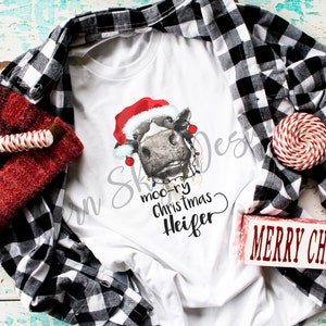 May include: White t-shirt with a black and white cow wearing a Santa hat and Christmas lights. The text "moo-ry christmas heifer" is written below the cow.