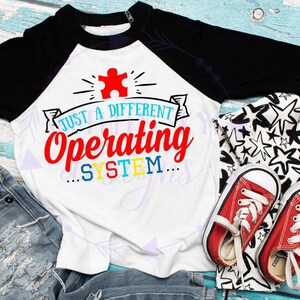May include: A white and black baseball tee shirt with a colorful puzzle piece and the text "Just a different operating system..." printed on the front. The shirt is being modeled on a child wearing blue jeans and red sneakers.