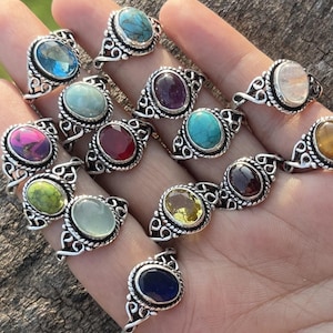 May include: A collection of 15 silver rings featuring different coloured gemstones. The rings have a delicate, ornate design with a small oval-shaped stone in the centre. The stones are a variety of colours, including red, blue, green, yellow, and purple.