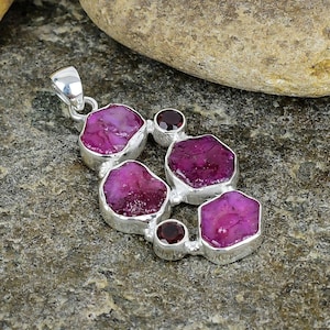 May include: A silver pendant featuring a cluster of six pink ruby gemstones, set in a silver frame. The pendant is accented with two smaller red gemstones.