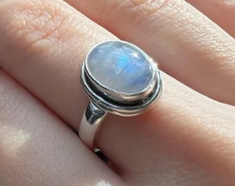 May include: A silver ring with a large oval moonstone set in a bezel setting. The ring has a simple band.