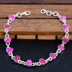 May include: A silver chain bracelet with pink oval-shaped gemstones. The bracelet has a lobster claw clasp.