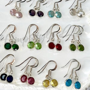 May include: Twelve pairs of silver dangle earrings with various coloured gemstones. The gemstones are round and about 6mm in diameter. The earrings are on a white surface.