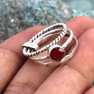 May include: A silver ring set with three bands, one of which is twisted. The top band features a red gemstone.