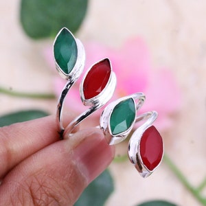 May include: Silver ring with a twisting design featuring alternating red and green gemstones.