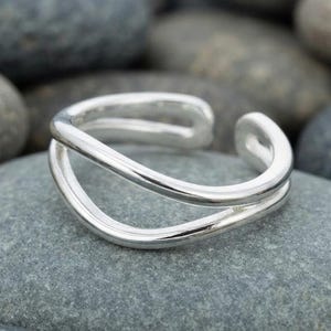 May include: A polished silver ring featuring an open, bypass-style design with two smooth, parallel bands that curve and overlap. The metal has a reflective, high-shine finish, creating a continuous, fluid shape that remains open at the front.