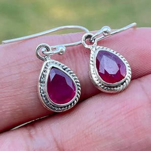 Puede incluir: Un par de pendientes de plata con piedras preciosas de rubí rojo en forma de lágrima.