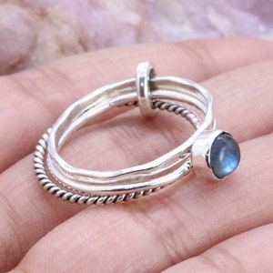 May include: A silver ring set with three bands, one with a twisted design and two smooth bands. The top band features a blue gemstone.
