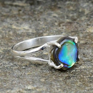 May include: A silver ring featuring a round iridescent abalone shell gemstone. The ring has a split band design.