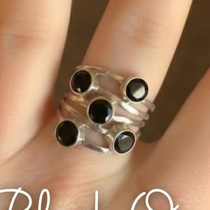 May include: A silver ring set with six black onyx stones. The ring is on a hand with long, oval nails, painted with a clear base and black star designs. The text "Black Onyx" is written in cursive.