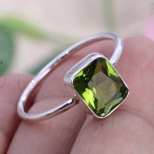 Puede incluir: Un anillo de plata con una piedra preciosa verde. La piedra preciosa es de corte cuadrado esmeralda.