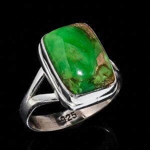 Pode incluir: Um anel de prata com uma pedra preciosa verde brilhante retangular com inclusões marrons. O anel tem um acabamento polido e um design de haste dividida. A banda é estampada com "925".