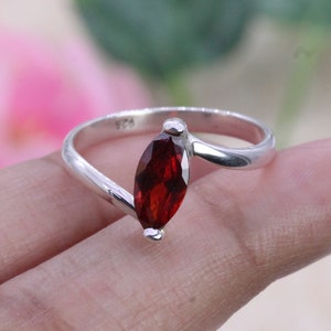 May include: A silver ring featuring a marquise-shaped red gemstone. The ring has a simple, elegant design.