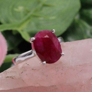 Peut inclure: Une bague en argent avec une grande pierre précieuse de rubis de forme ovale. Le rubis est de couleur rouge foncé et a une taille facetée.