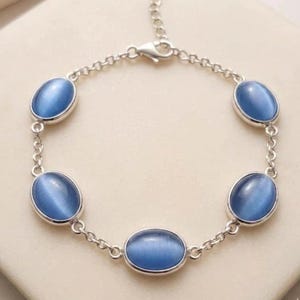 May include: A silver-toned bracelet featuring five oval, light blue gemstones. The gemstones are set in individual bezels and connected by a delicate chain. The bracelet has an adjustable clasp.