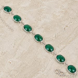 May include: A silver bracelet featuring oval-cut, vibrant green gemstones. The gemstones are set in individual bezels and linked together with a delicate chain. The bracelet has a secure clasp closure and is displayed on a neutral surface.