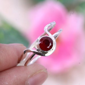 以下が含まれることがあります： 渦巻き模様に赤い宝石がセットされたシルバーリング