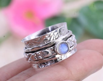 May include: A silver spinning ring with a moonstone gemstone. The ring has a floral design and is made of multiple bands.
