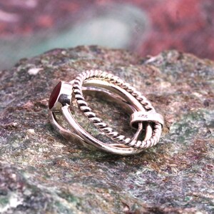 May include: A silver ring featuring a red gemstone and a twisted band design. The ring is marked with the number "925" on the side.