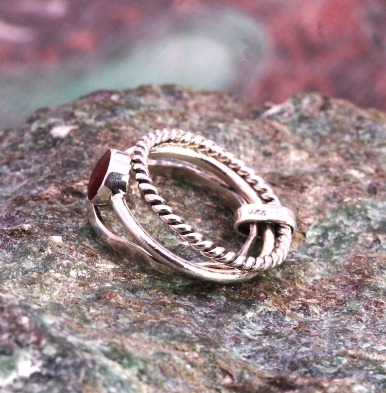 May include: A silver ring featuring a red gemstone and a twisted band design. The ring is marked with the number "925" on the side.