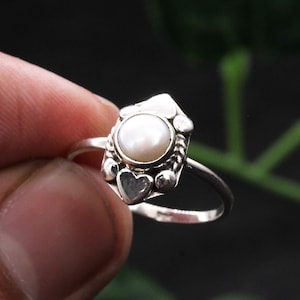 Op de afbeelding: Een zilveren ring met een witte parel in een hartvormig ontwerp.