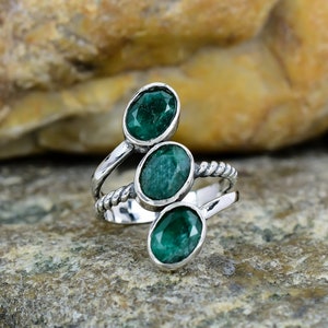 May include: A silver ring with three green oval-shaped gemstones. The ring has a twisted band.