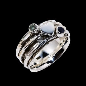 May include: A silver ring featuring a heart-shaped central stone and two smaller, round gemstones. The ring has a textured band and is set against a black backdrop. The ring is a piece of jewellery.